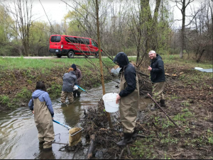 Participants gather next to the street to collect sample. A couple people are in knee deep water and one person is giving at thumbs up.